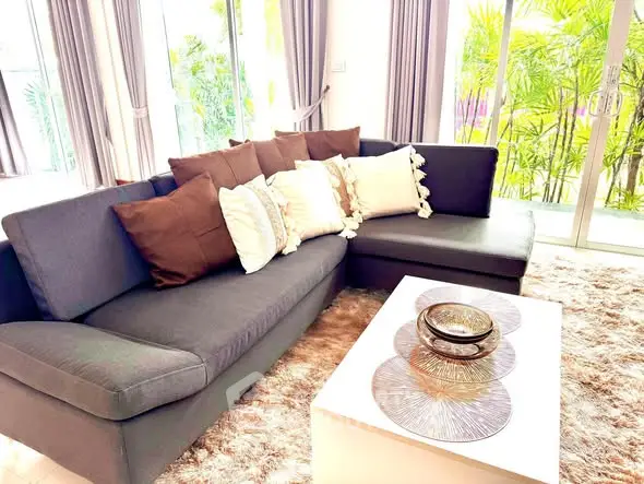 Luxurious living room with plush sofa and elegant decor, featuring large windows and lush greenery view.