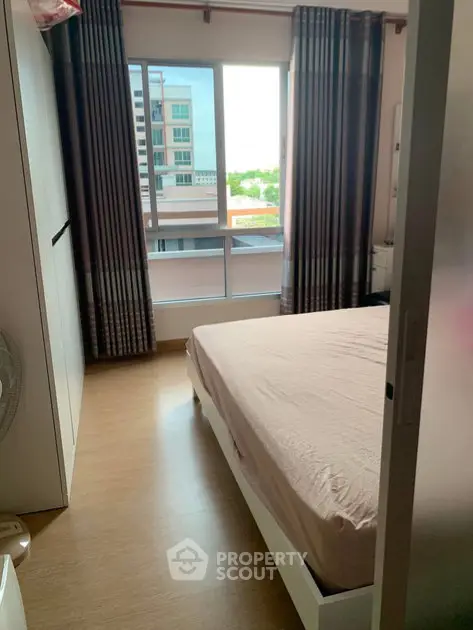 Cozy bedroom with large window offering natural light and city view, perfect for relaxation.