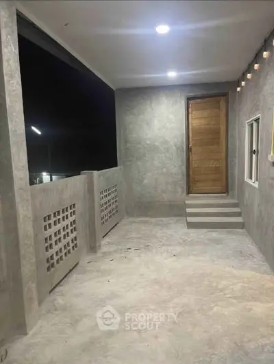 Modern concrete balcony with ambient lighting and wooden door at night.