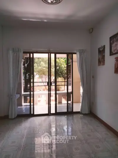 Spacious living room with large glass doors leading to a balcony, offering natural light and garden view.
