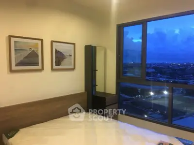 Modern bedroom with large window offering stunning city view at dusk, featuring stylish decor and cozy ambiance.