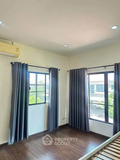 Bright bedroom with large windows and wooden flooring, featuring modern curtains and air conditioning.