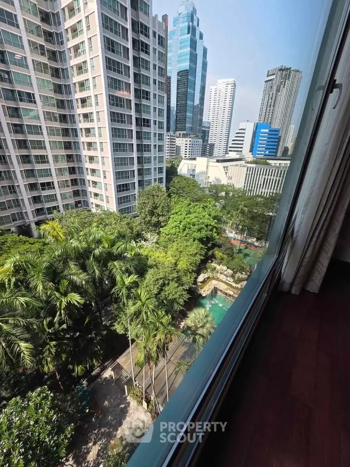 Stunning cityscape view from high-rise apartment window overlooking lush greenery and modern skyscrapers.