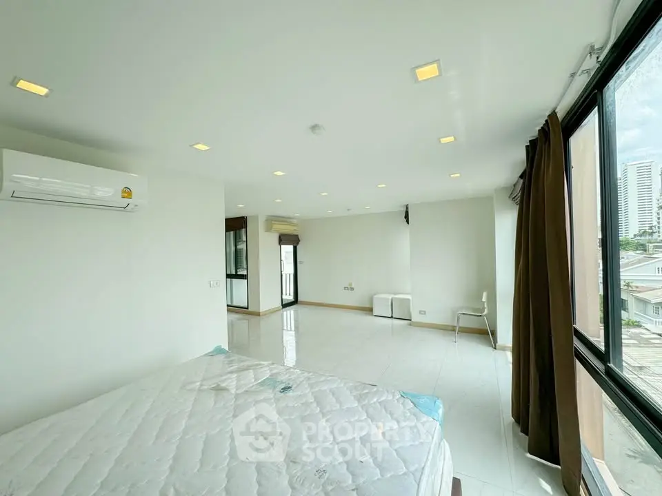 Spacious bedroom with large windows and city view, featuring modern lighting and air conditioning.