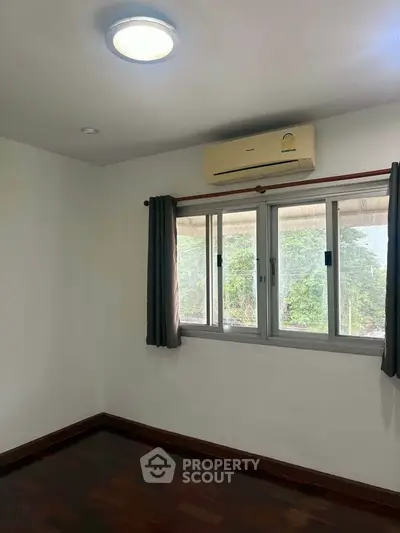 Bright bedroom with large window and air conditioning, featuring wooden flooring and neutral decor.