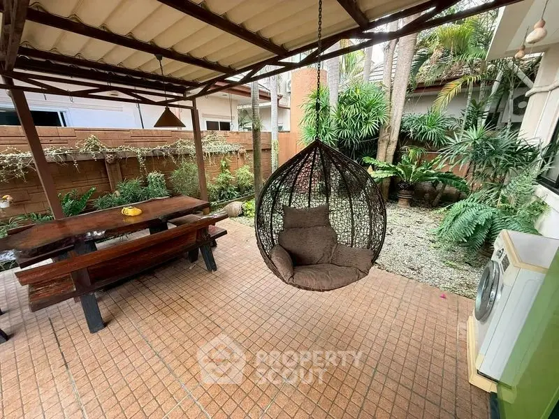 Charming outdoor patio with hanging chair and lush greenery, perfect for relaxation and entertaining.