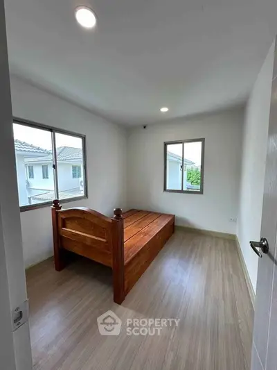Spacious bedroom with wooden bed and large windows offering natural light