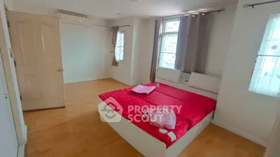 Spacious bedroom with red bedding and natural light from multiple windows.