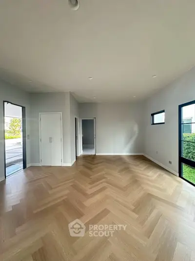 Spacious modern living room with herringbone wood flooring and large windows offering natural light.