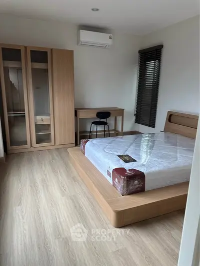 Modern bedroom with wooden flooring, stylish bed, and sleek wardrobe in a bright, airy space.
