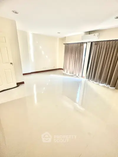 Spacious empty room with glossy floors and large windows for natural light.