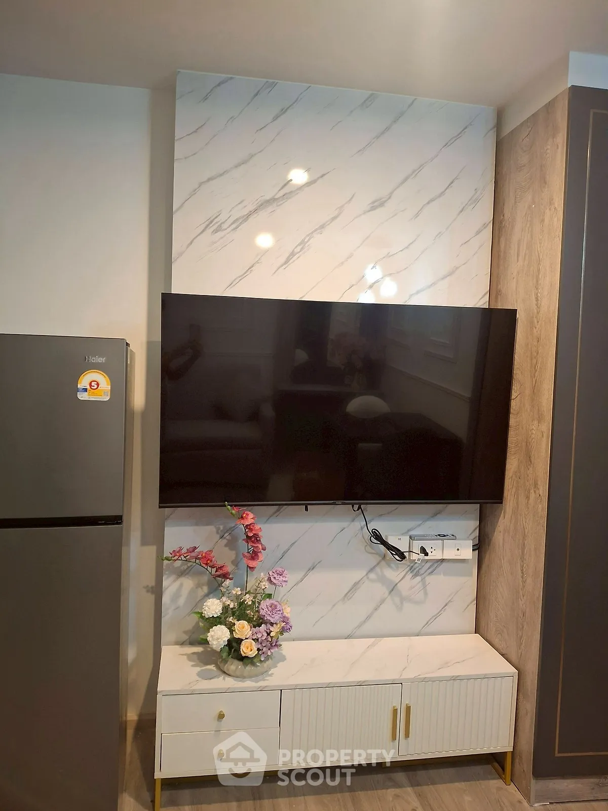 Modern living room with marble accent wall and mounted TV, featuring sleek cabinetry and floral decor.