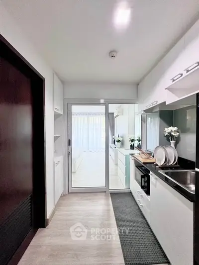 Modern kitchen with sleek white cabinets and black countertop, leading to a bright living area.