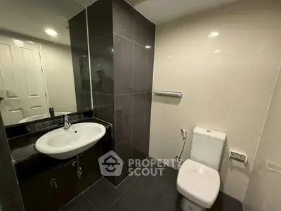 Modern bathroom with sleek black and white tiles, featuring a stylish sink and toilet.