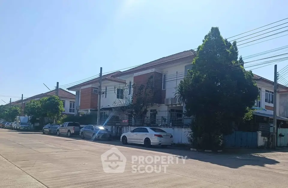 Charming suburban street with modern townhouses and parked cars under a clear blue sky.
