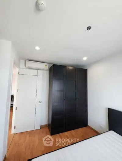 Modern bedroom with sleek black wardrobe and wooden flooring, featuring a minimalist design and bright lighting.