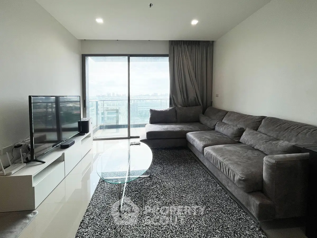 Spacious modern living room with large sectional sofa and floor-to-ceiling windows offering stunning city views.