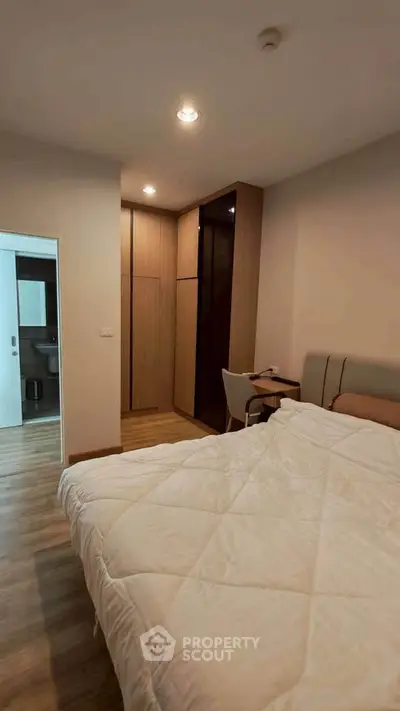 Cozy bedroom with modern decor and wooden flooring, featuring a comfortable bed and a small study area.