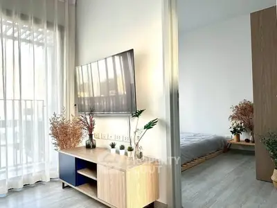 Modern living room with stylish decor and natural light, featuring a sleek TV setup and cozy bedroom view.