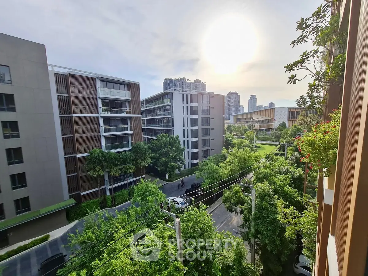 Stunning urban view from a modern apartment balcony overlooking lush greenery and contemporary buildings.
