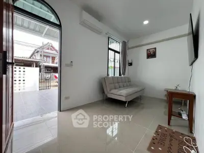 Modern living room with sleek sofa and wall-mounted TV, open to a bright entrance.