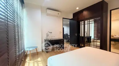 Spacious bedroom with modern furnishings and natural light, featuring a desk and large windows with blinds.