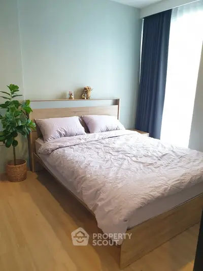 Cozy bedroom with wooden flooring and large window, featuring a comfortable bed and stylish decor.