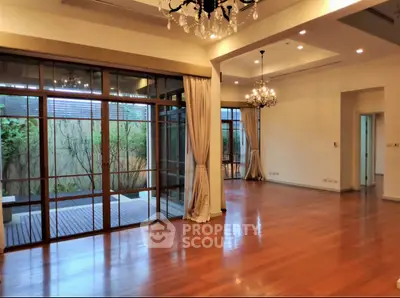 Spacious living room with elegant chandeliers and large windows opening to a private deck.