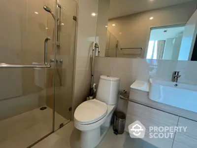 Modern bathroom with glass shower enclosure, sleek vanity unit, and well-placed lighting creating a bright and inviting space.