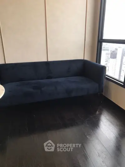 Modern living room with dark wood flooring and a stylish blue sofa near a large window with city view.