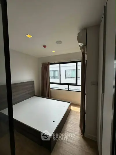 Modern bedroom with large window and wooden flooring in a stylish apartment.