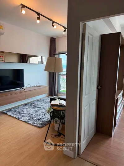 Modern living room with stylish decor and large TV, featuring a cozy rug and elegant lighting.