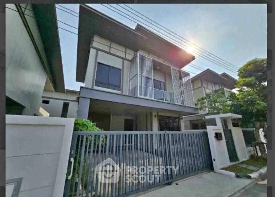 Modern two-story house with sleek design and gated entrance in a suburban neighborhood.