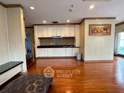 Spacious living room with elegant wooden flooring and modern kitchen cabinetry.
