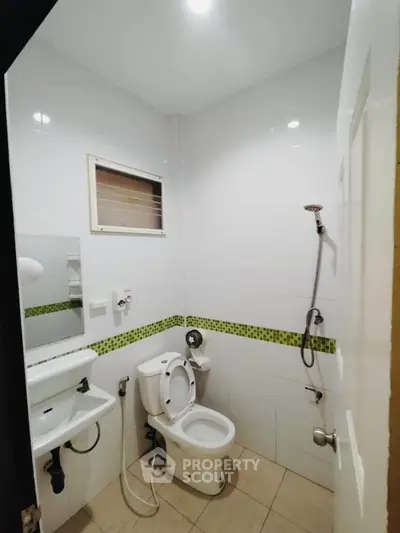 Modern bathroom with white tiles and green accents, featuring a shower and toilet in a compact layout.