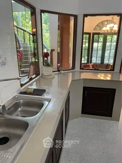 Spacious kitchen with dual sinks and large windows overlooking lush greenery