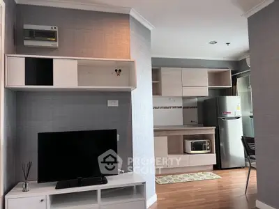 Modern living room with TV and compact kitchen featuring microwave and fridge in open layout.