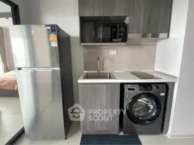 Modern compact kitchen with stainless steel fridge, microwave, and washing machine in sleek apartment.