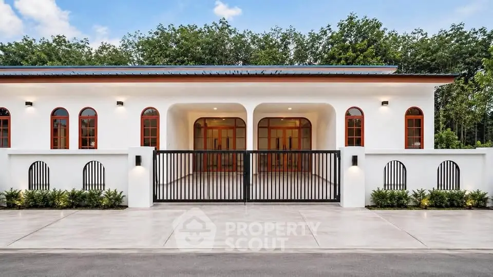 Stunning modern villa with arched windows and gated entrance, surrounded by lush greenery.