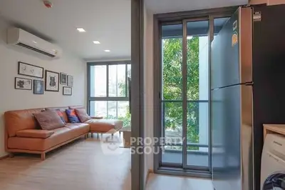 Modern living room with leather sofa and large windows next to a sleek kitchen area with stainless steel fridge.