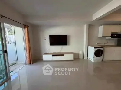 Spacious living room with modern TV setup and washing machine, featuring open layout and natural light.