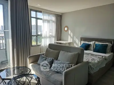 Modern studio apartment with cozy living area and large windows offering city views.
