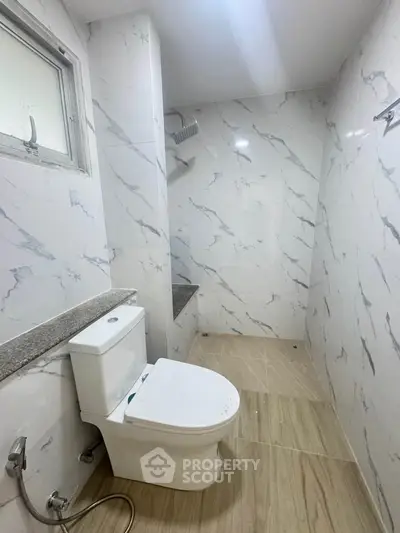 Modern bathroom with marble walls and wooden flooring, featuring a sleek toilet and shower area.
