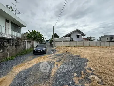 Vacant land plot with gravel driveway and surrounding residential houses.
