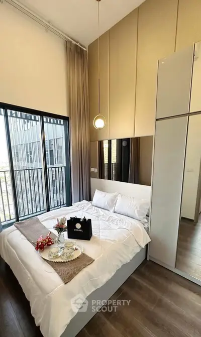 Modern bedroom with high ceiling and large window, featuring elegant decor and natural light.