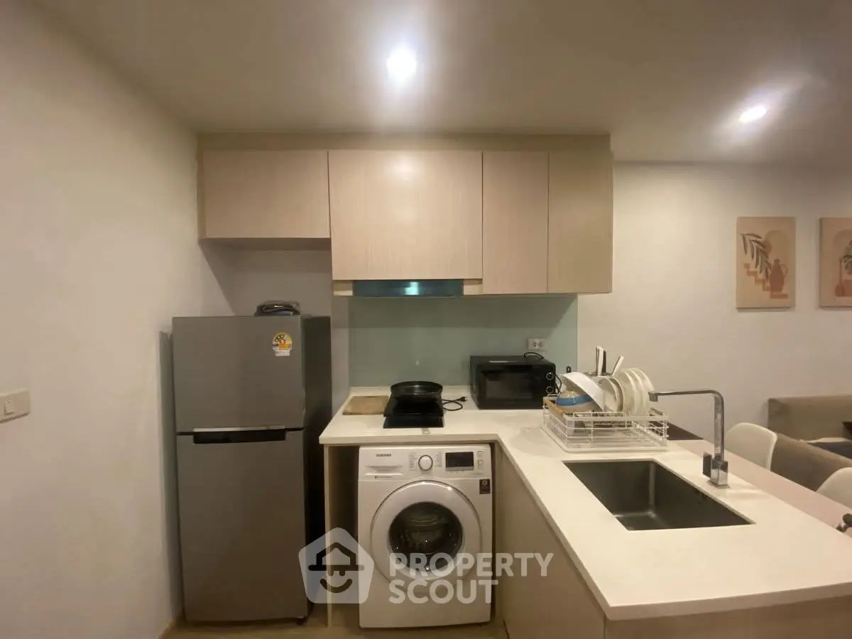 Modern kitchen with washing machine, fridge, and sleek cabinetry in a cozy apartment setting.