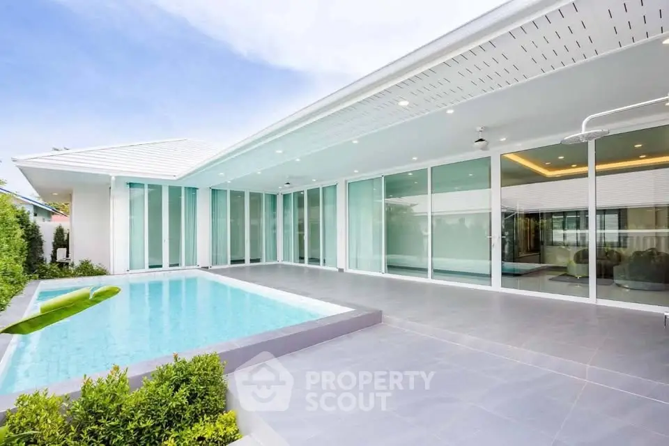 Modern luxury villa with sleek design and private pool, featuring expansive glass walls and lush greenery.