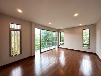 Spacious living room with hardwood floors and large windows overlooking greenery.
