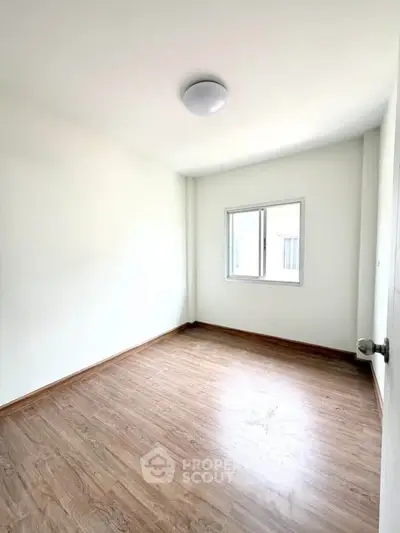 Bright empty room with wooden flooring and a window, perfect for customization.