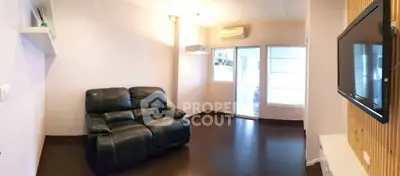 Modern living room with sleek black leather sofa and wall-mounted TV, featuring dark wood flooring.